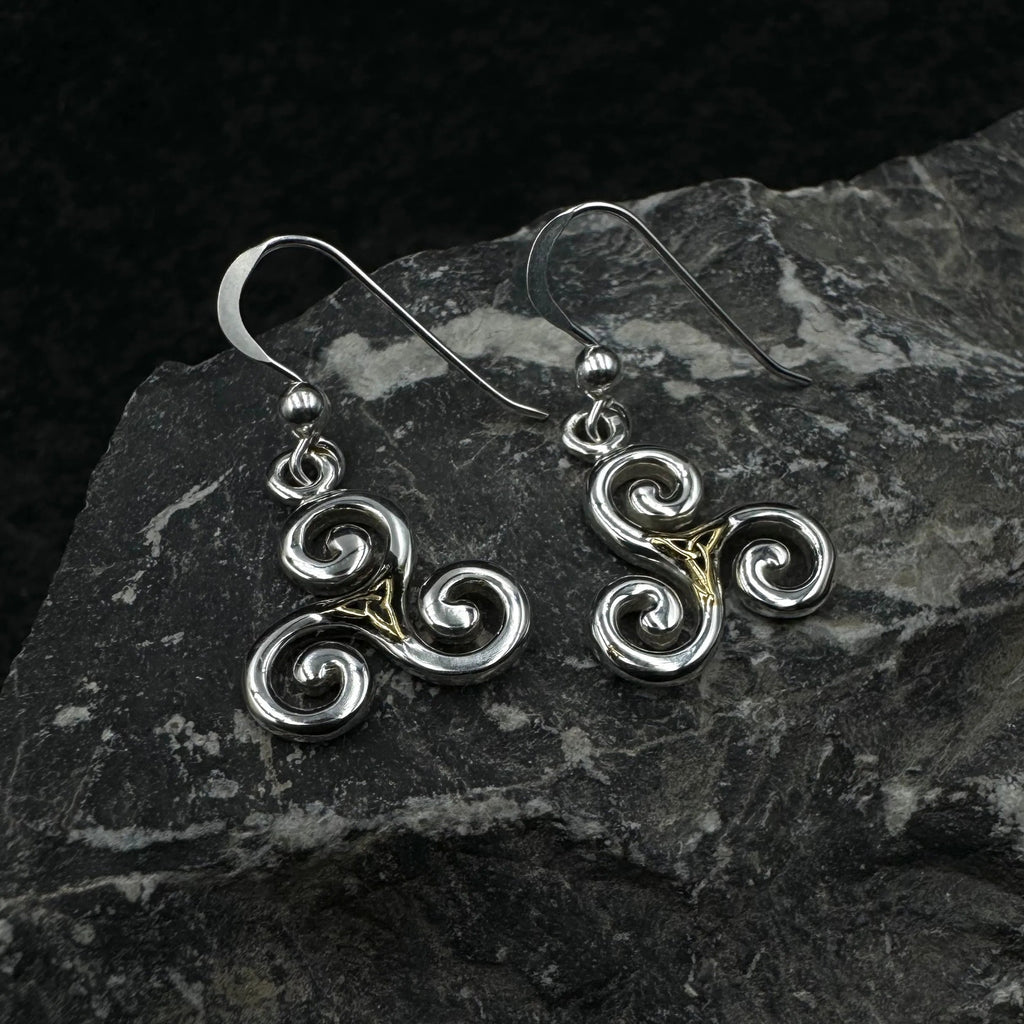 Pair of silver and gold Celtic spiral earrings on a dark stone surface