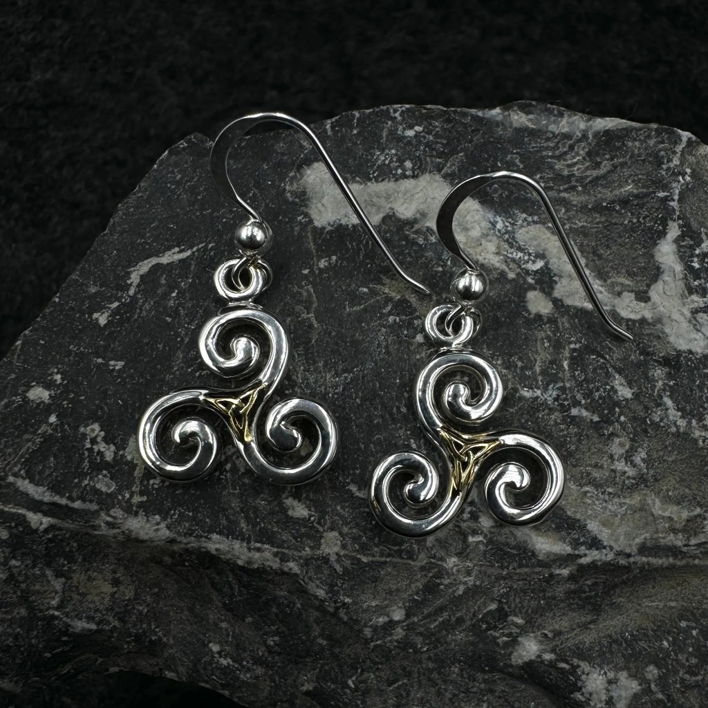Pair of silver and gold Celtic spiral earrings on a dark stone surface