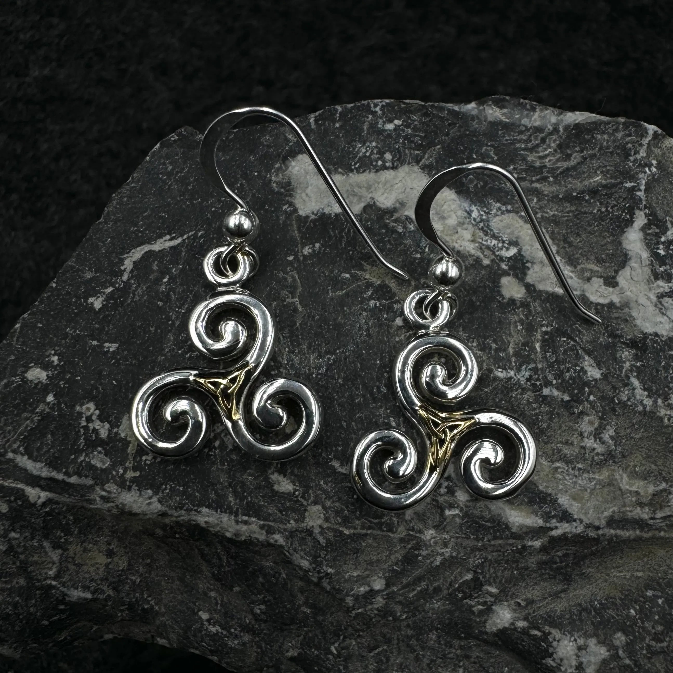 Pair of silver and gold Celtic spiral earrings on a dark stone surface