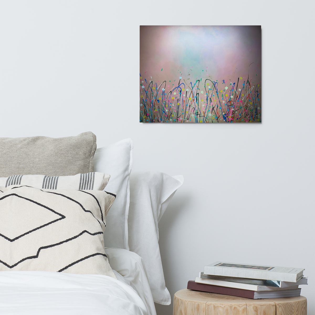 Abstract flower painting on a wall above a bed with pillows and books.