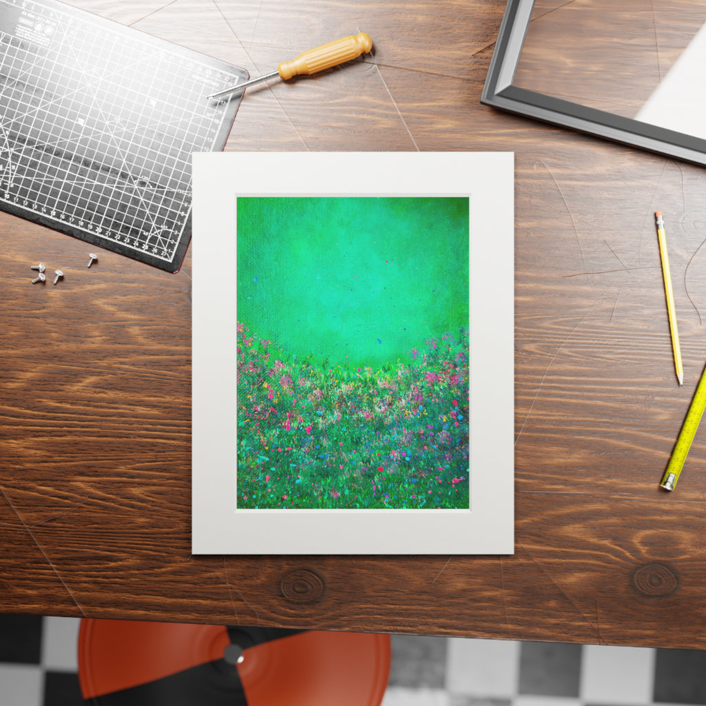 A framed art print featuring a vibrant green and blue floral landscape, displayed on a dark wood desk surrounded by creative tools like a cutting mat, pencil, and screwdriver.